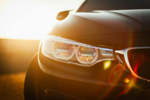 Sunlit close-up of a sleek modern car headlight with a lens flare effect at sunset.